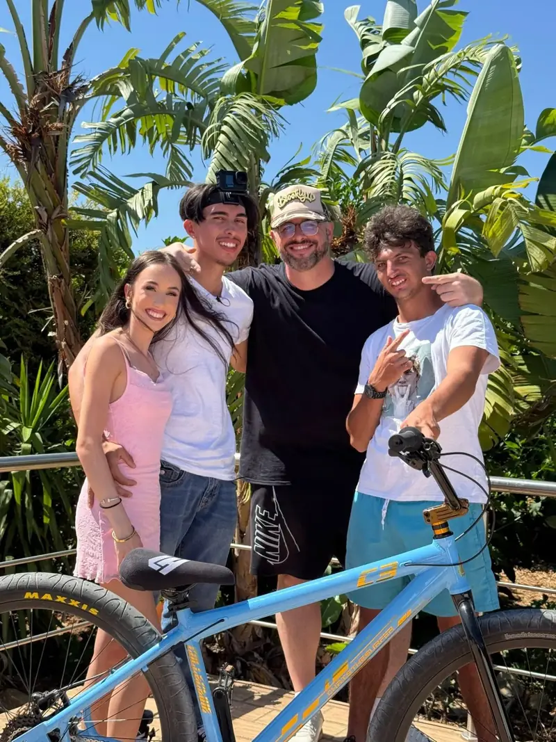 Four people standing arm in arm behind a blue mountain bike under palm and banana trees