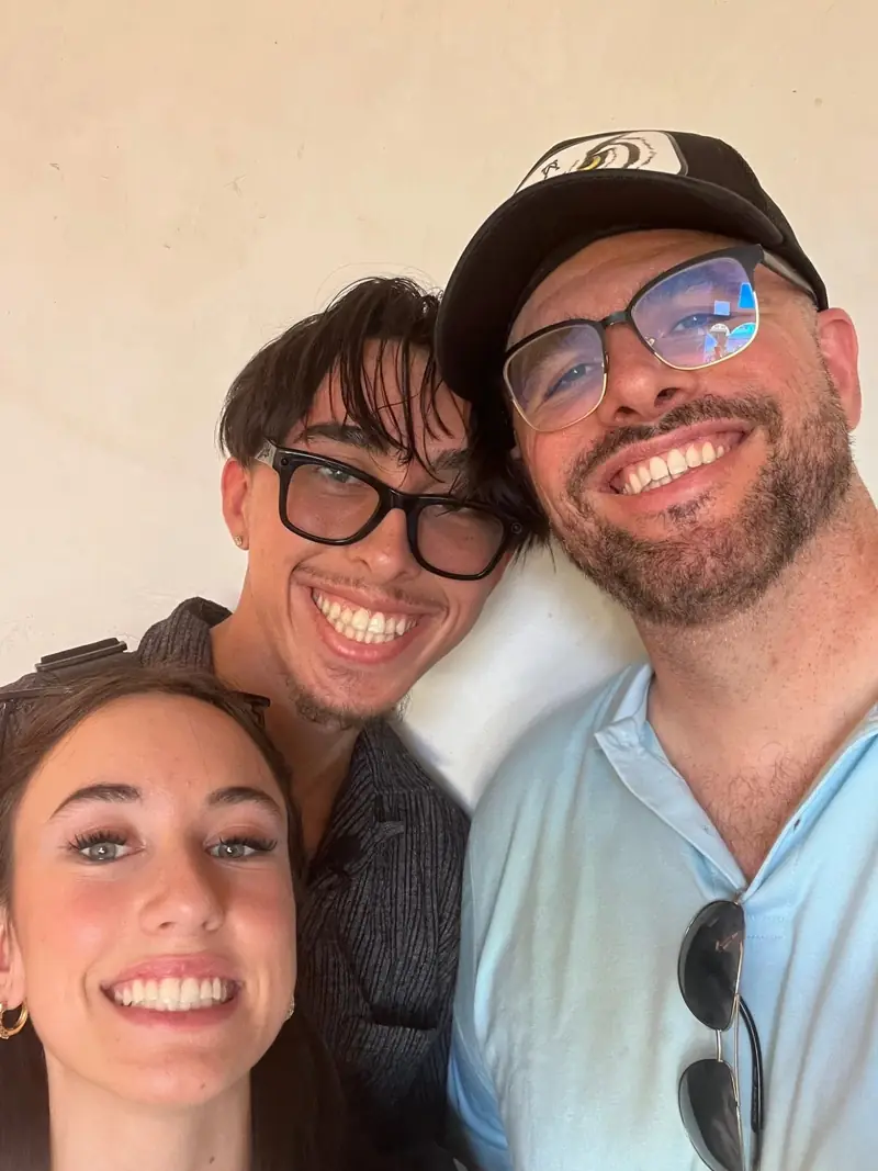 A close selfie of three smiling people, two of them wearing glasses