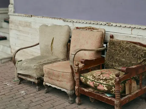 Three worn armchairs standing outdoors on brick paving against a wall