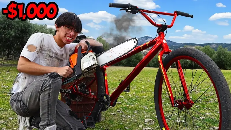 Christopher Maddaloni Jr. crouched behind a red bike in a park, holding a chainsaw to its frame