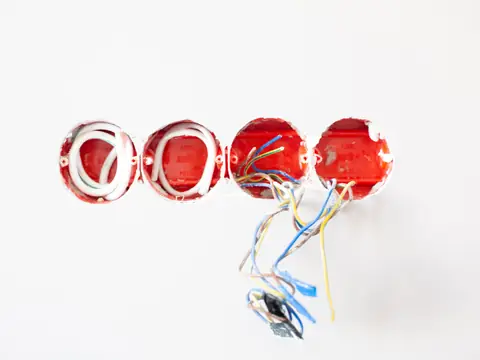 Four red wall boxes in a white wall with coloured wires hanging from one of them