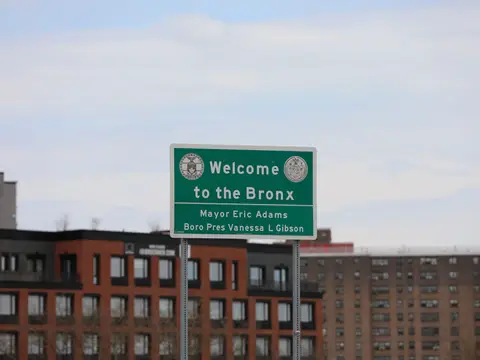 A green road sign reading Welcome to the Bronx above brick apartment buildings