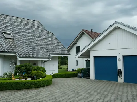 White houses with two blue garage doors and a paved forecourt around a clipped hedge