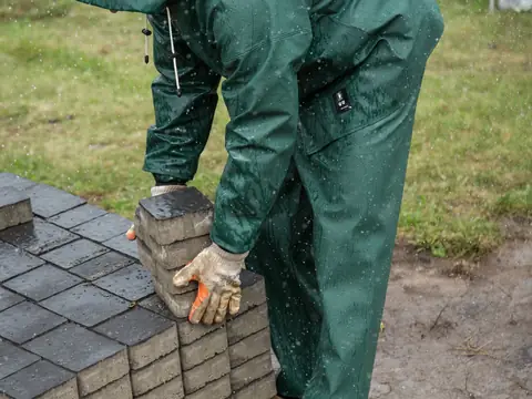 A worker in green overalls and gloves lifting grey paving blocks from a stack