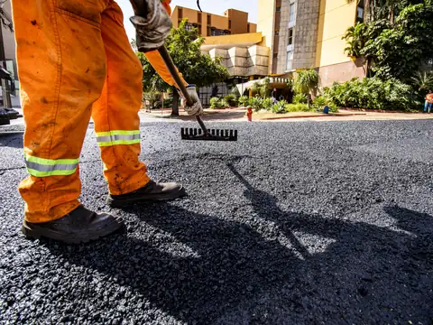 A worker in orange trousers with reflective bands raking fresh black asphalt level