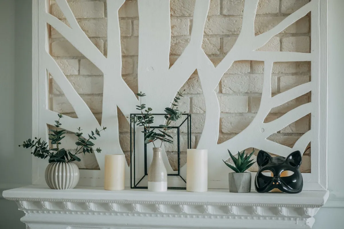 A stylish mantel display with candles, vases, plants, and a decorative mask, reflecting modern design trends.